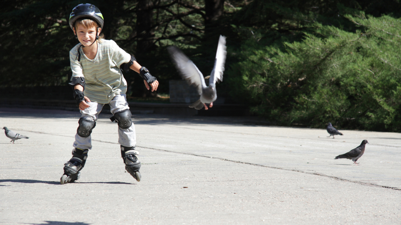 Мальчик катается на роликах на асфальте с голубями