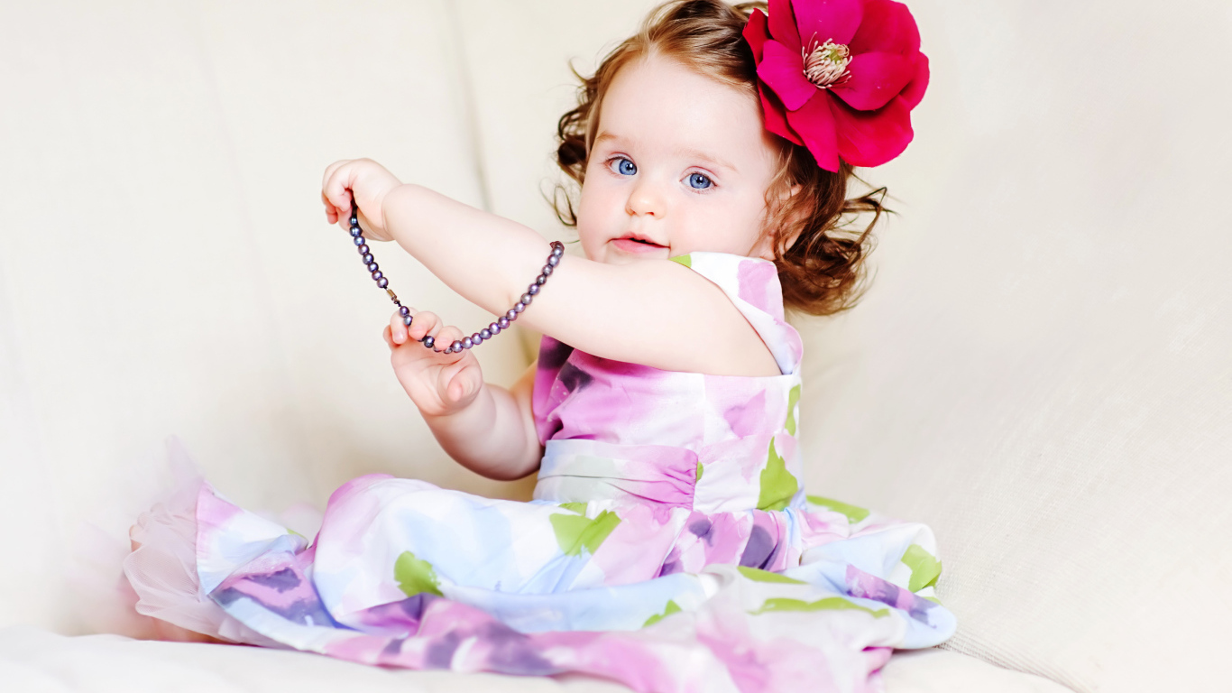 Милая голубоглазая малышка с большим красным цветком в волосах