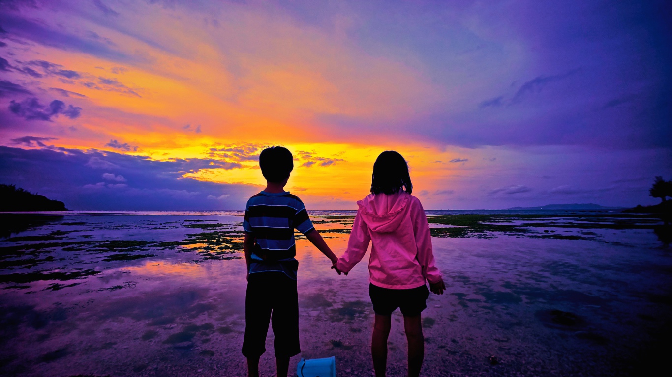 Маленькие мальчик и девочка стоят у воды на фоне заката 