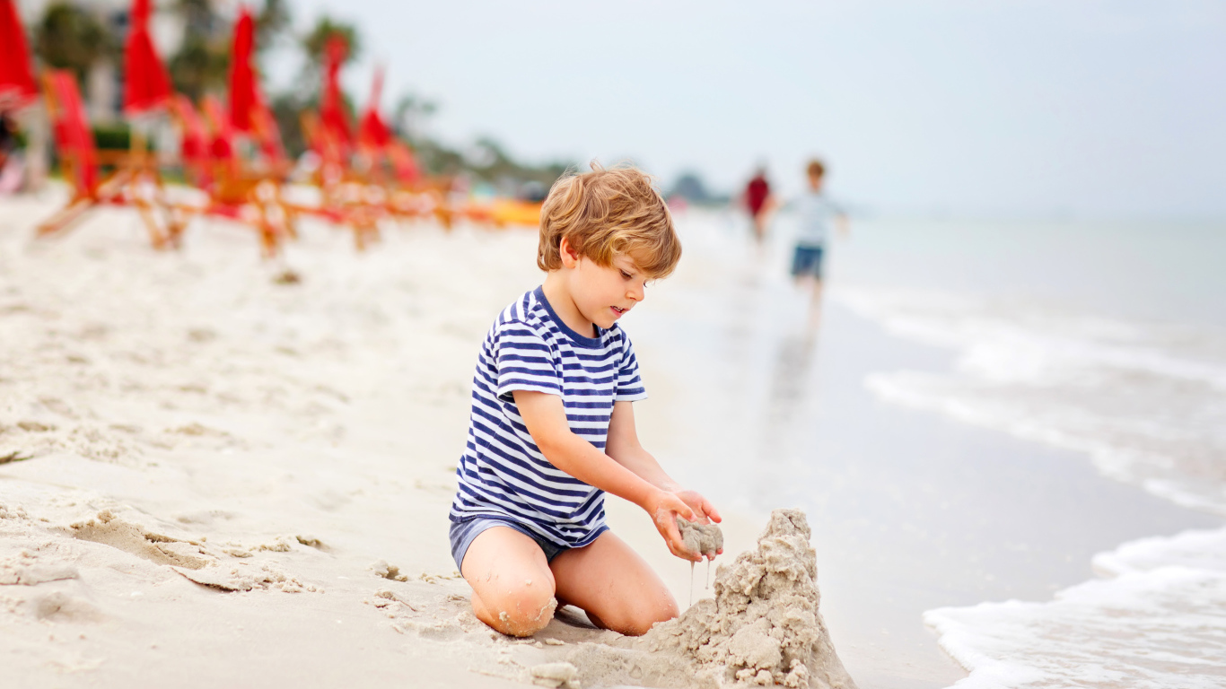Маленький мальчик строит замок из песка на пляже