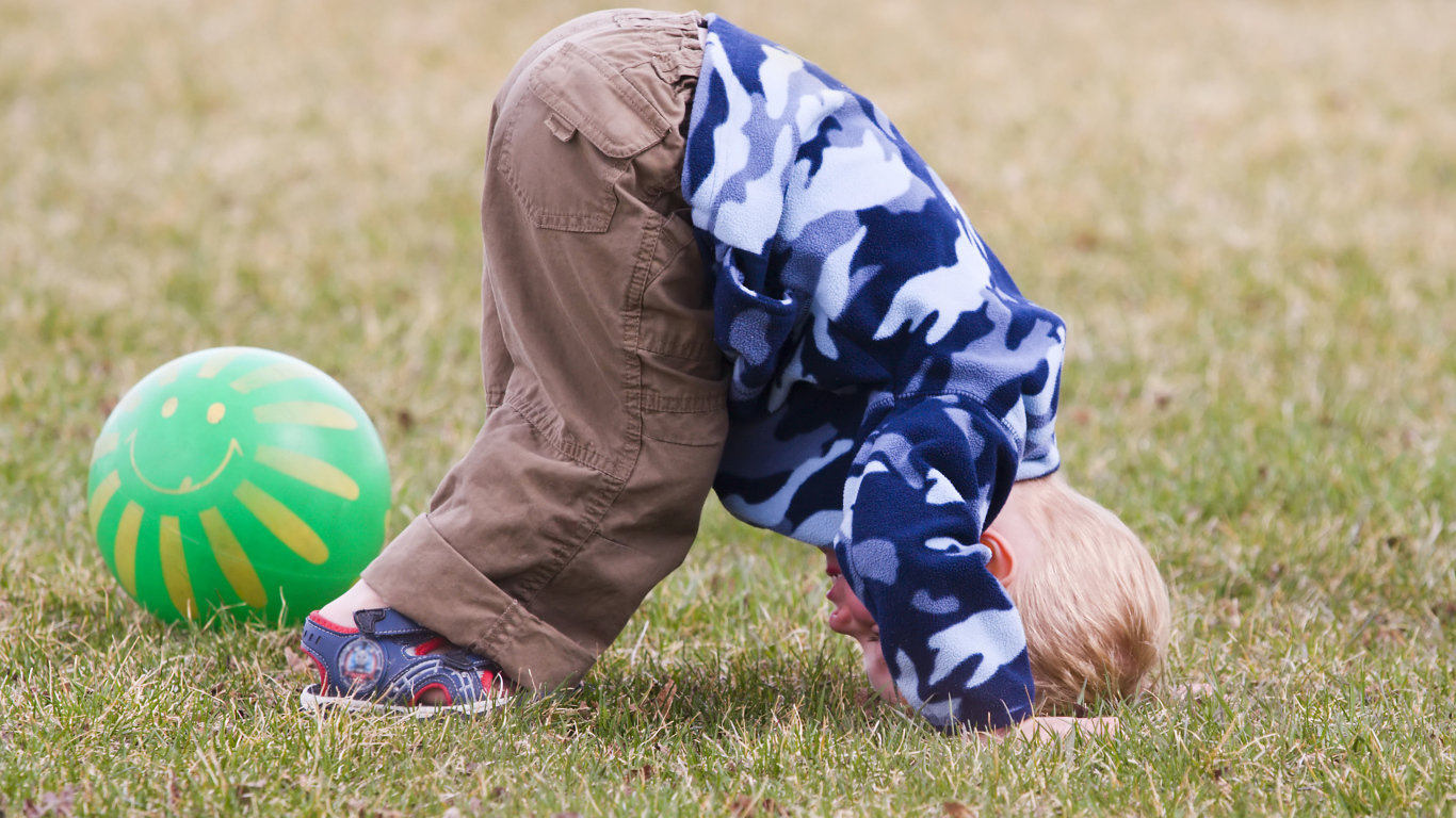 Маленький мальчик играет на траве с мячом