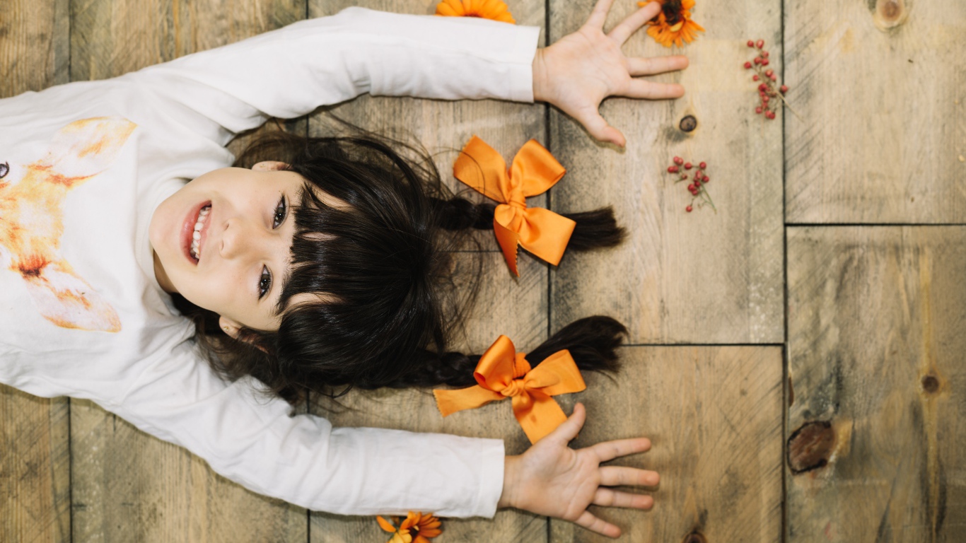 Маленькая веселая девочка с косичками лежит на полу