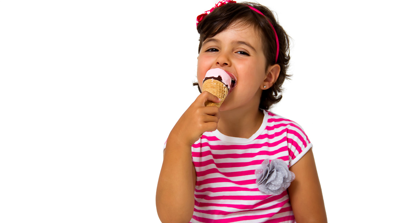 Маленькая девочка ест мороженое за столом на белом фоне