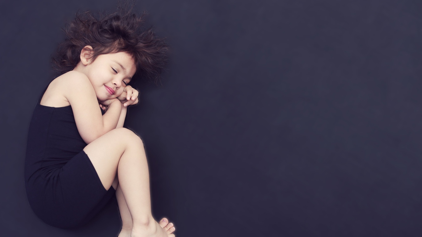 Маленькая девочка в черном платье спит на черном фоне