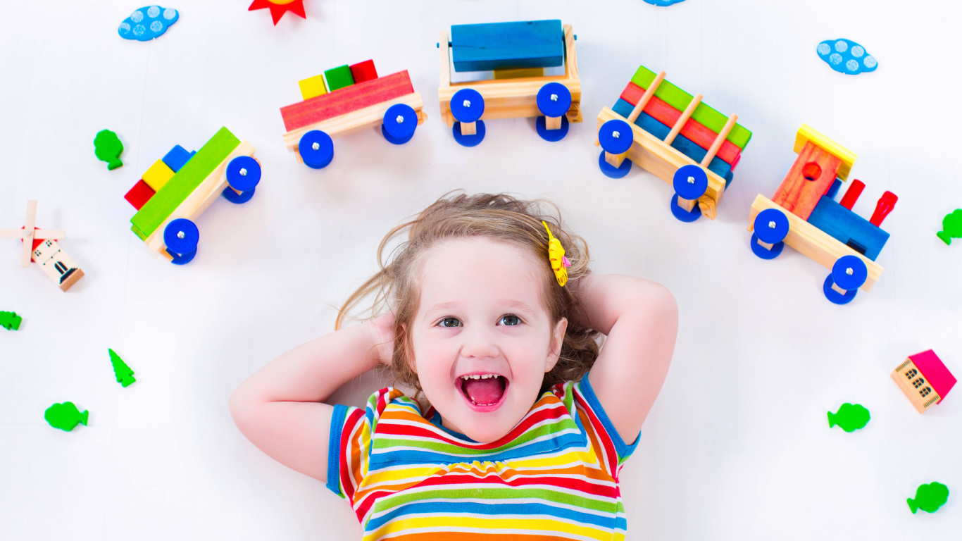 Маленькая девочка на сером фоне с игрушечным паровозом 