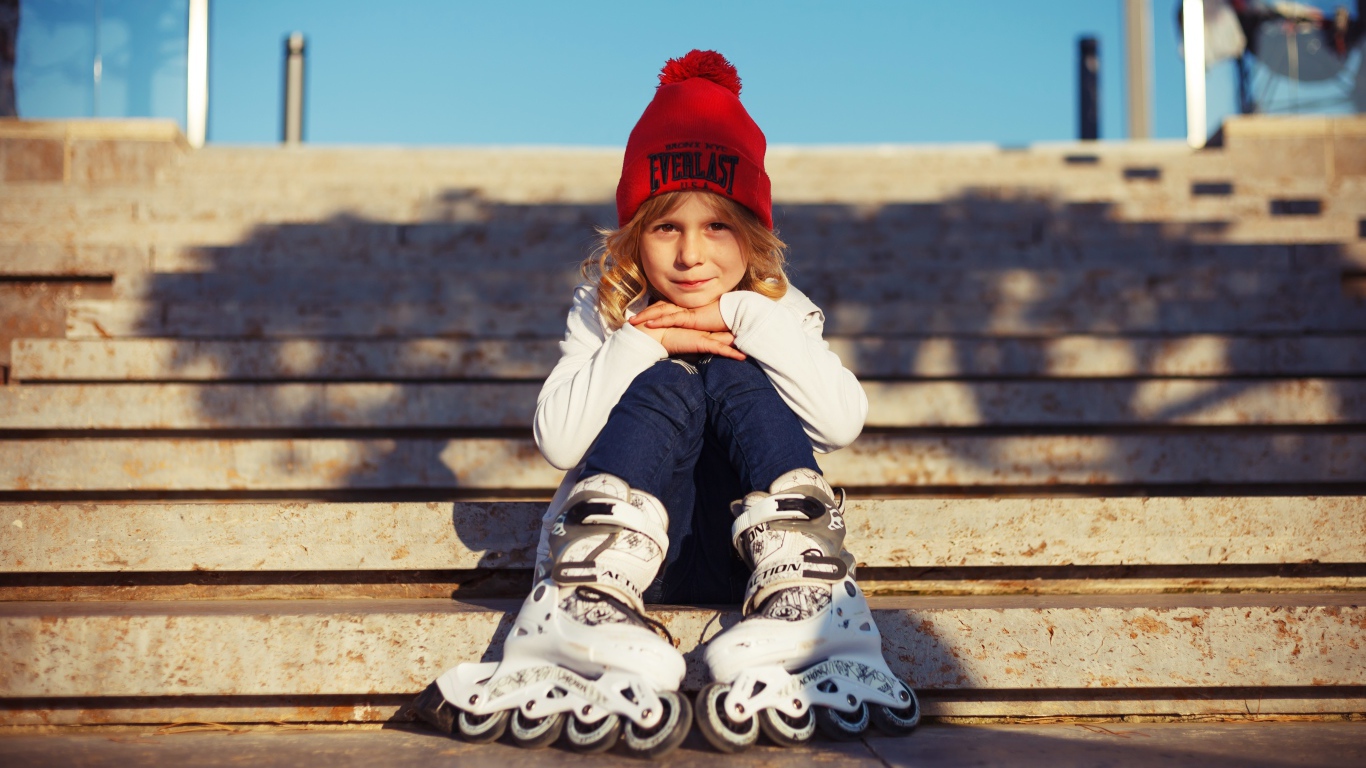 Маленькая девочка в роликах сидит на ступеньках 