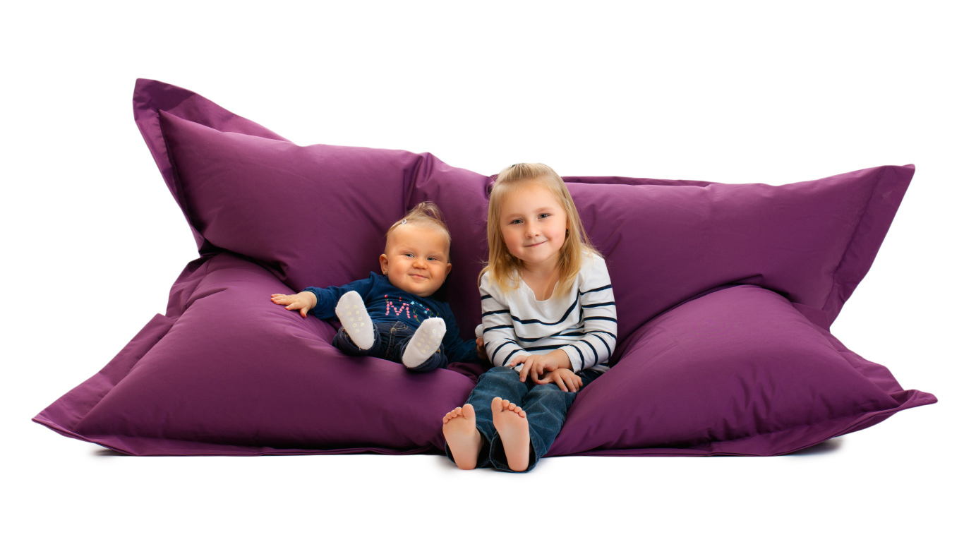 Маленькие девочки сидят на мягкой подушке на белом фоне