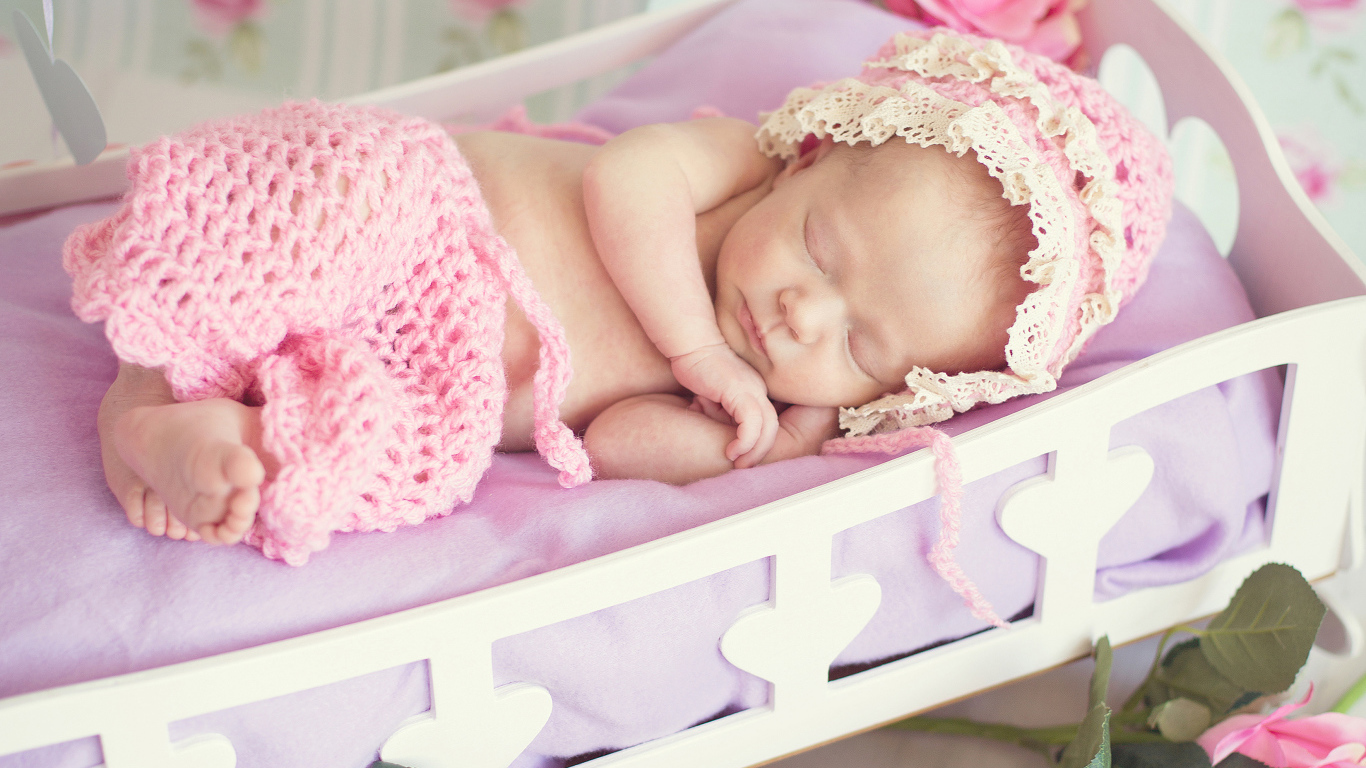 Спящий ребенок в розовом вязаном костюме в колыбели