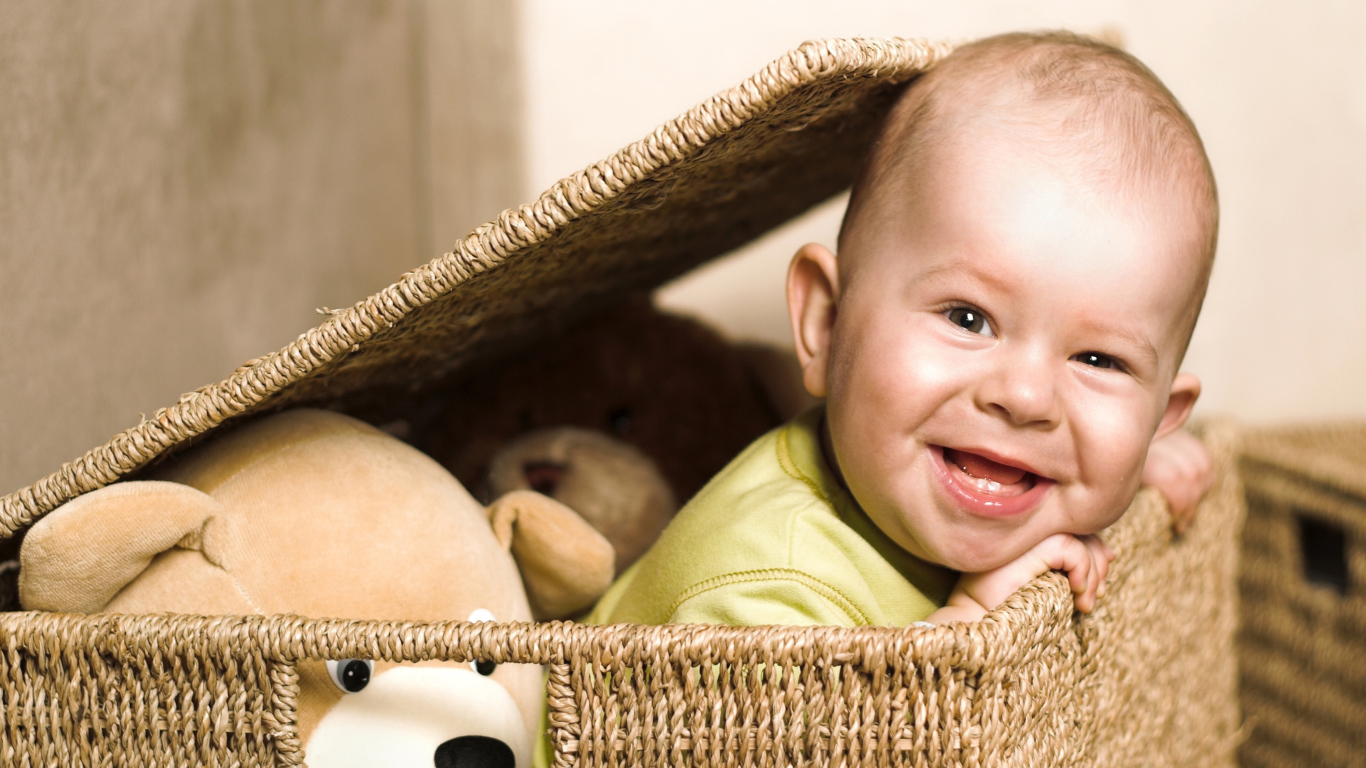 Улыбающийся забавный малыш в плетеной корзине с игрушками