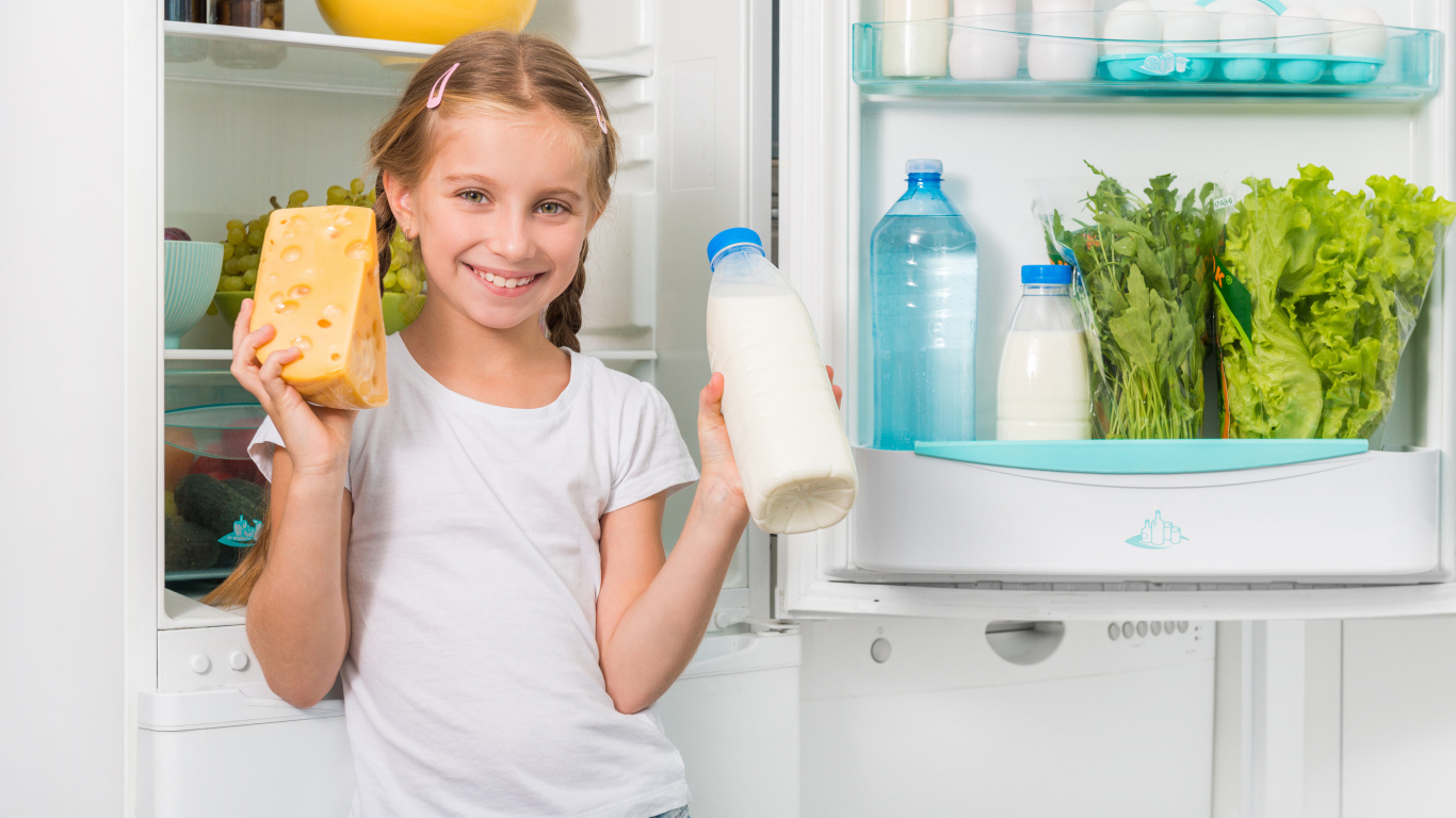 Улыбающаяся девочка у холодильника с сыром и молоком