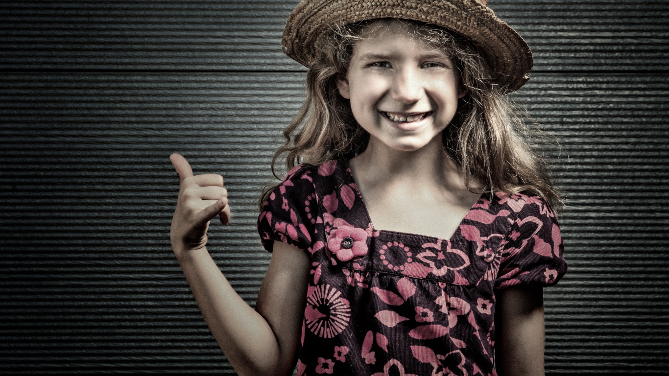 Улыбающаяся девочка в соломенной шляпе у стены 