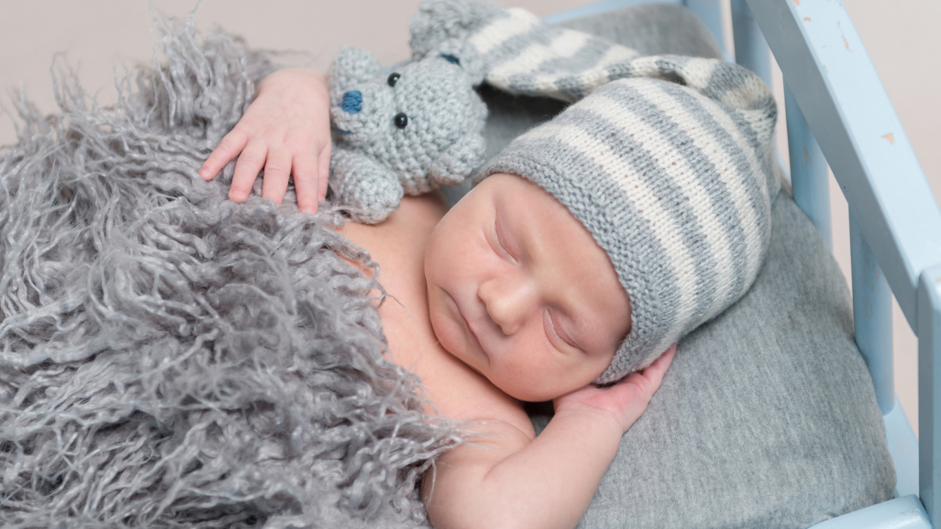 Младенец в вязаной шапке спит с игрушкой под меховым одеялом