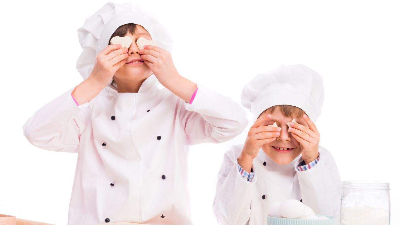 Два маленьких мальчика в костюмах повара на кухне делают печенье