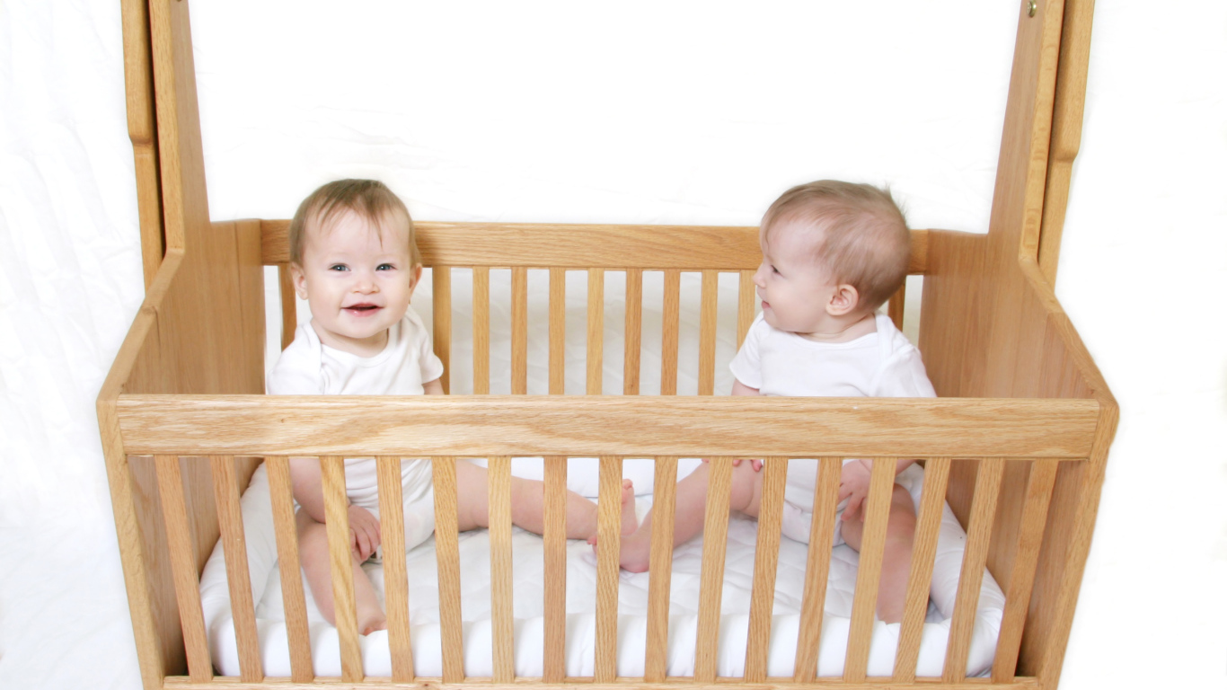 Два улыбающихся малыша в деревянной кроватке