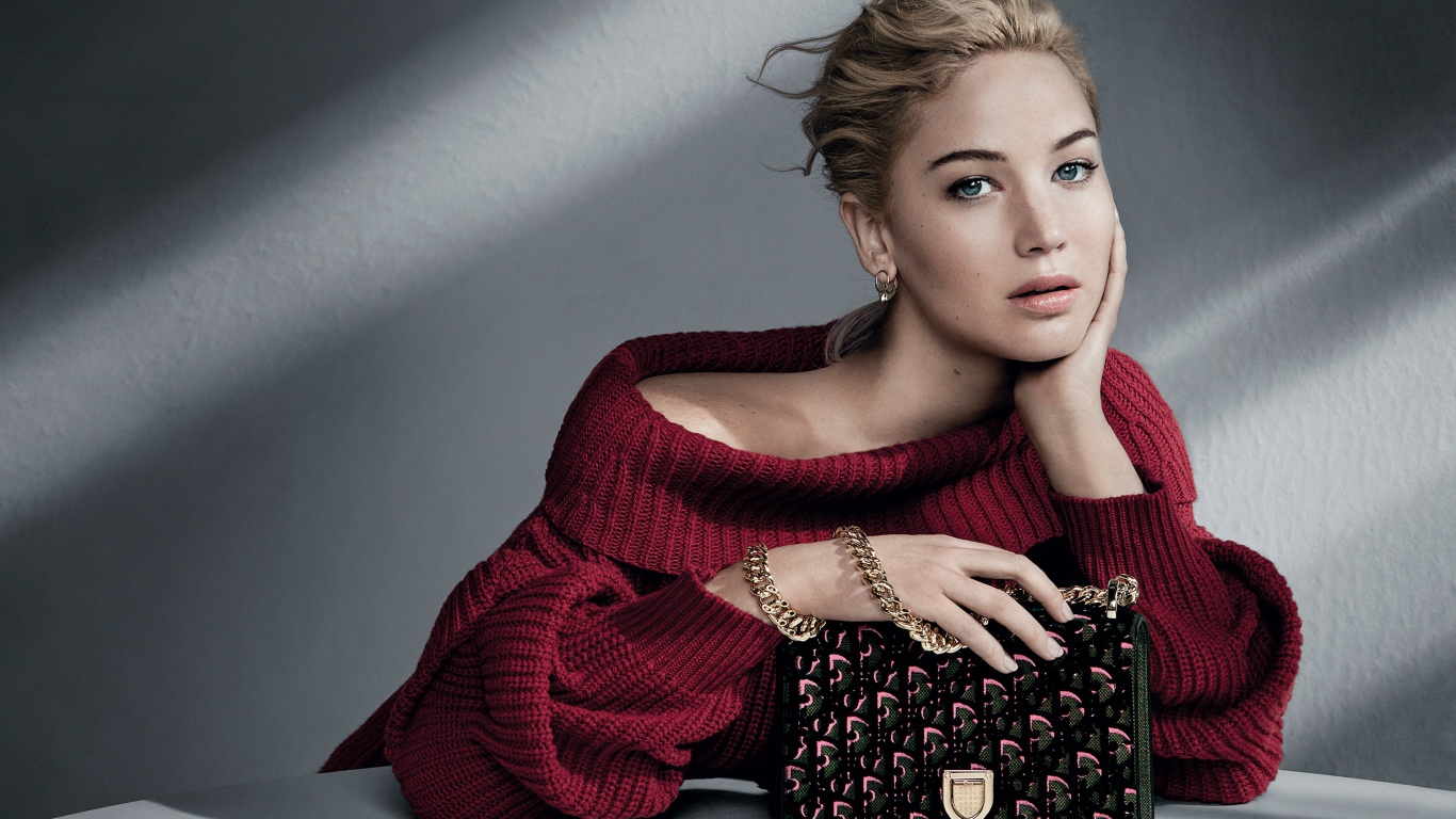 Актриса Дженнифер Лоуренс в красном свитере с сумочкой на сером фоне