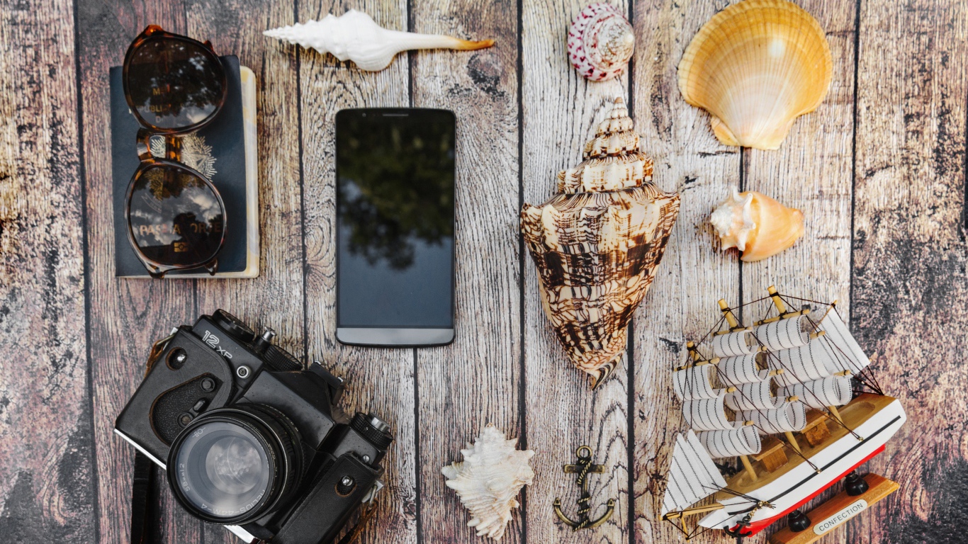 Фотоаппарат, смартфон, ракушки, очки и паспорт на столе
