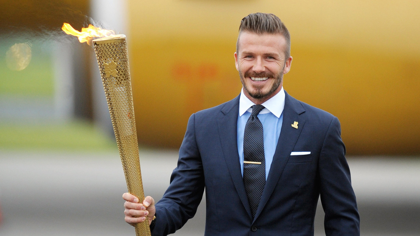 Улыбающийся футболист Дэвид Бекхэм с олимпийский огнем в руке