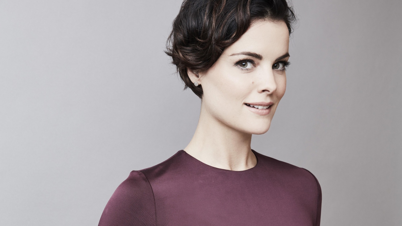 Улыбающаяся девушка, актриса Джейми Александр на сером фоне