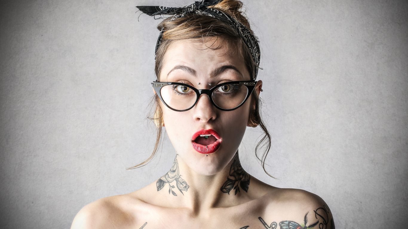 Удивленная девушка в очках с татуировками на теле