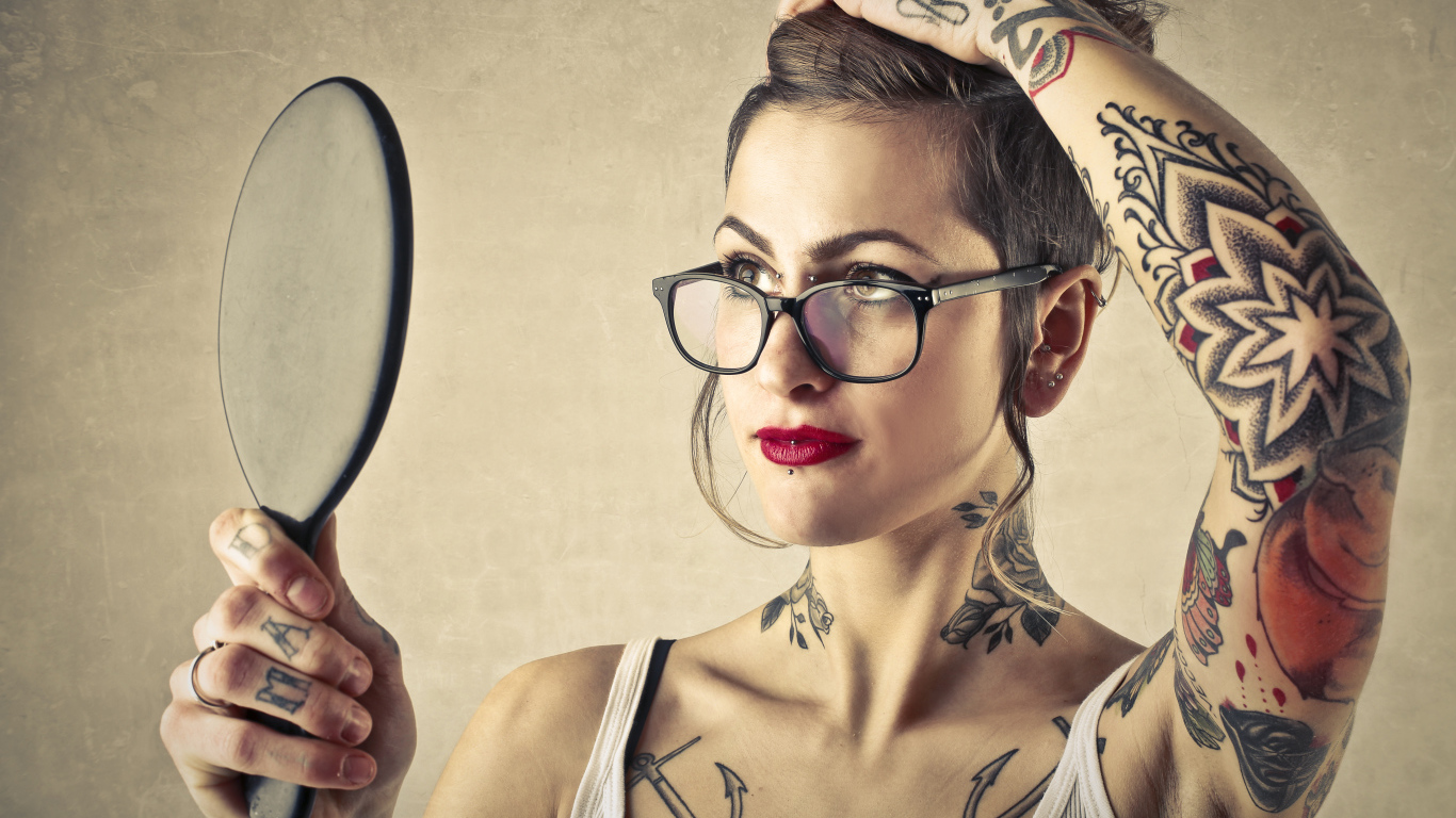 Девушка с татуировками на теле смотрит в зеркало