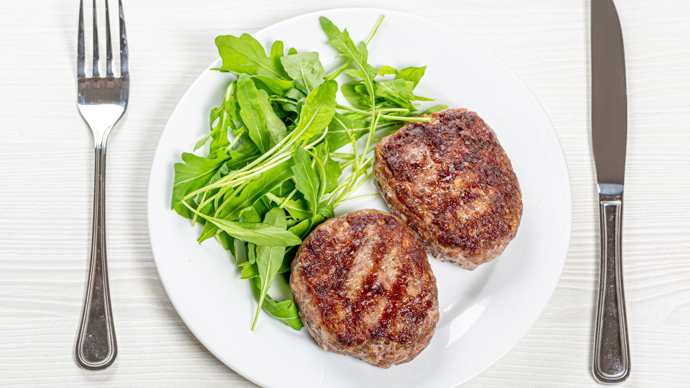 Две котлеты на тарелке с зеленью рукколы 