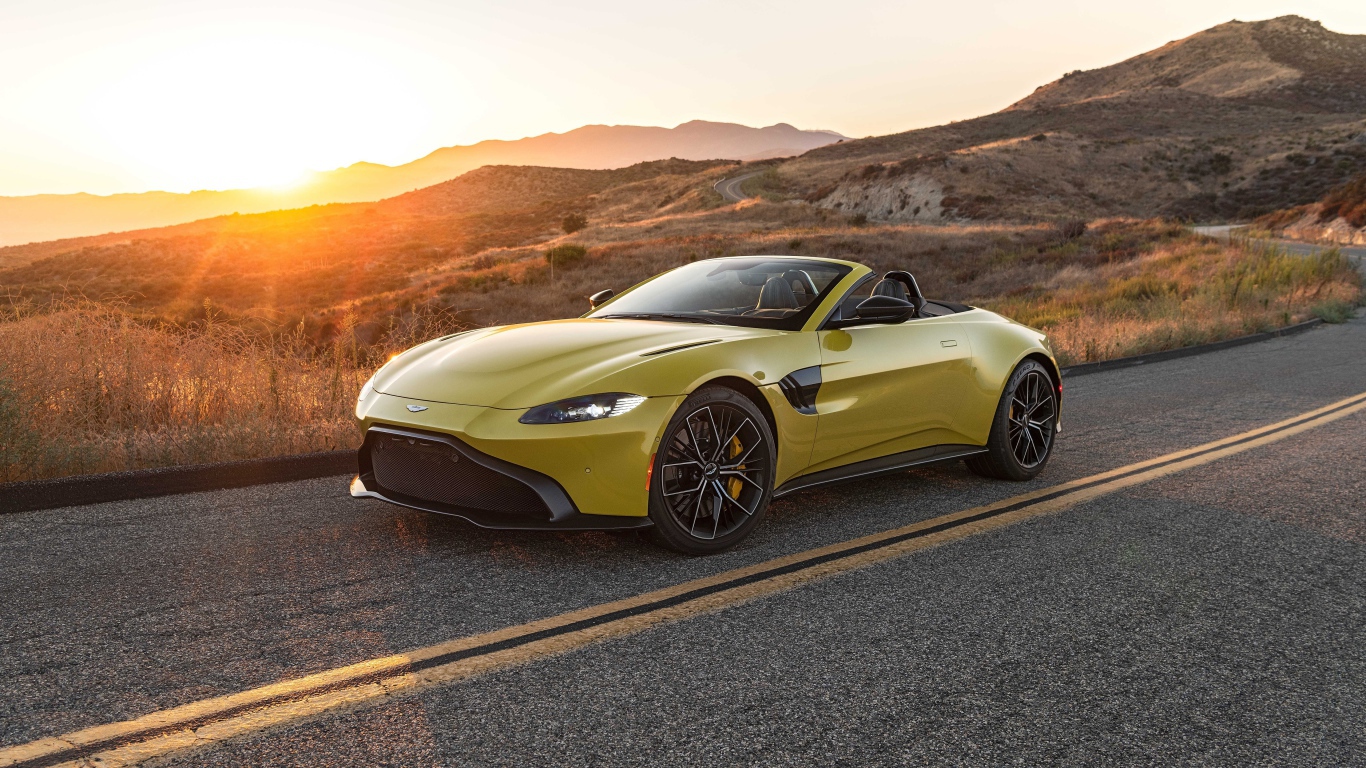 Желтый кабриолет  Aston Martin Vantage Roadster, 2021 года на трассе на рассвете