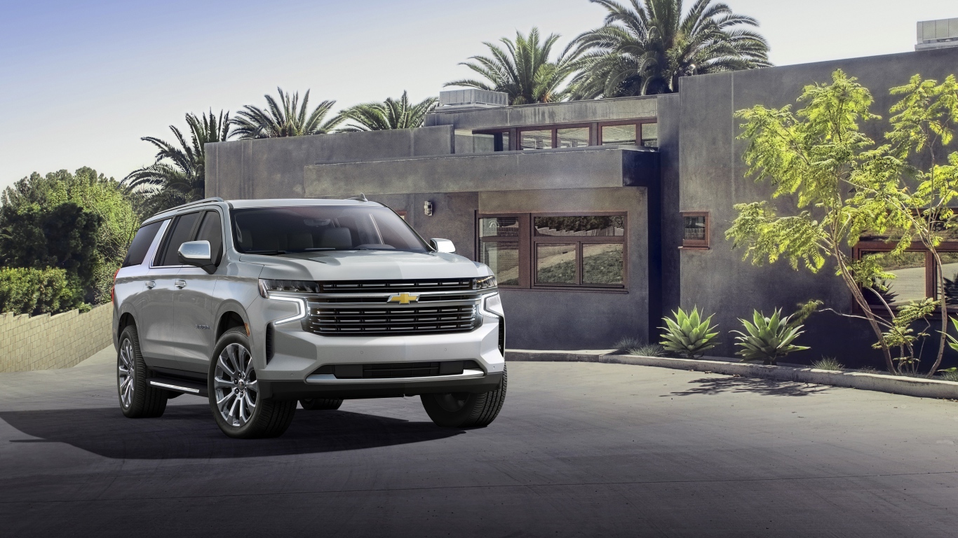 Серый внедорожник Chevrolet Suburban, 2021 года на фоне дома