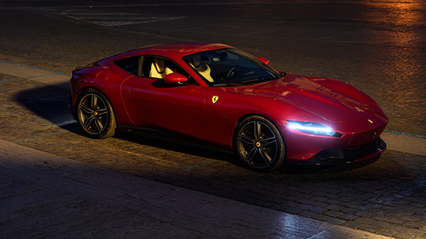 Красный автомобиль Ferrari Roma 2020 года с включенными фарами вечером