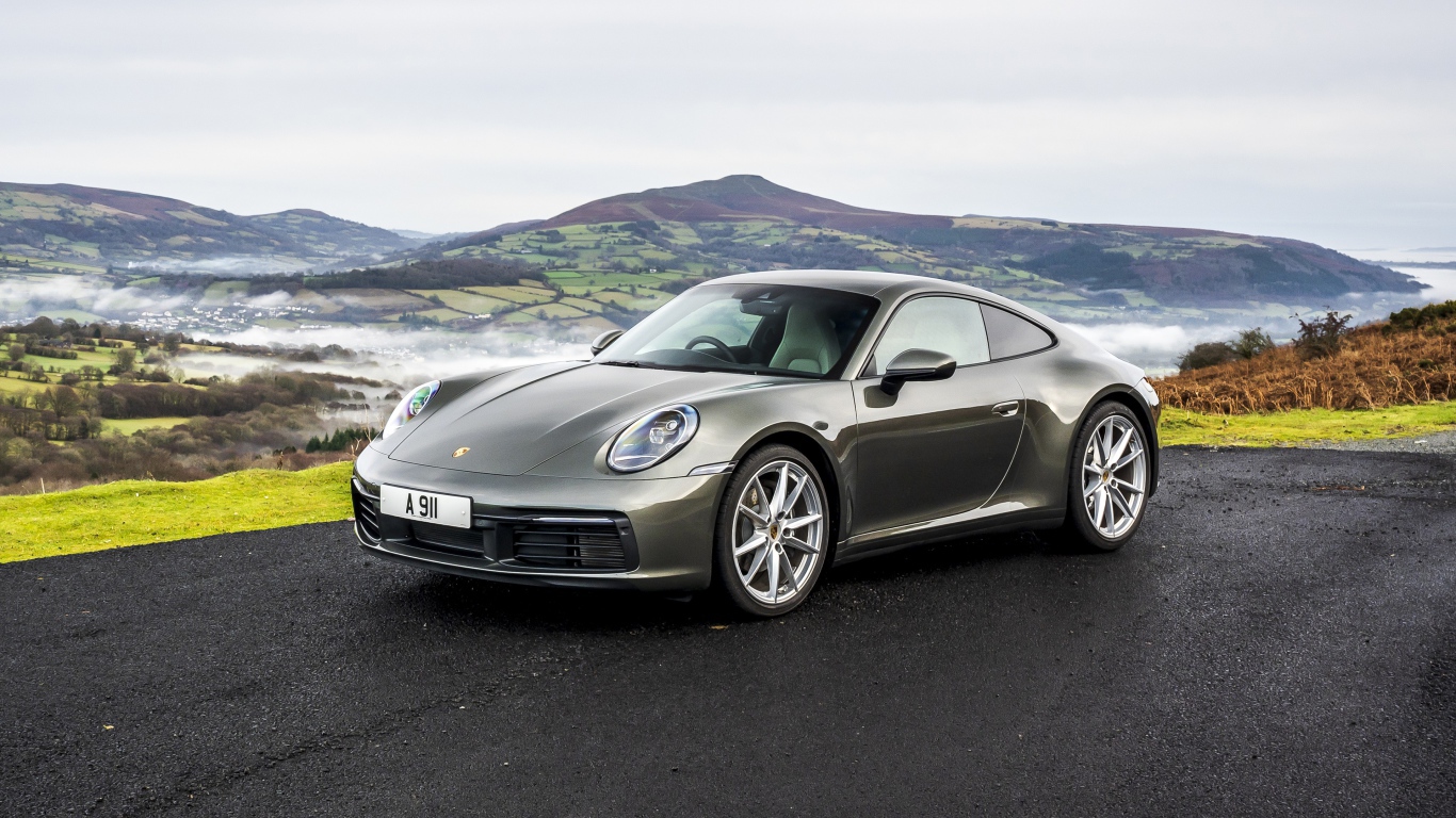 Серебристый автомобиль Porsche 911 Carrera на фоне холмов