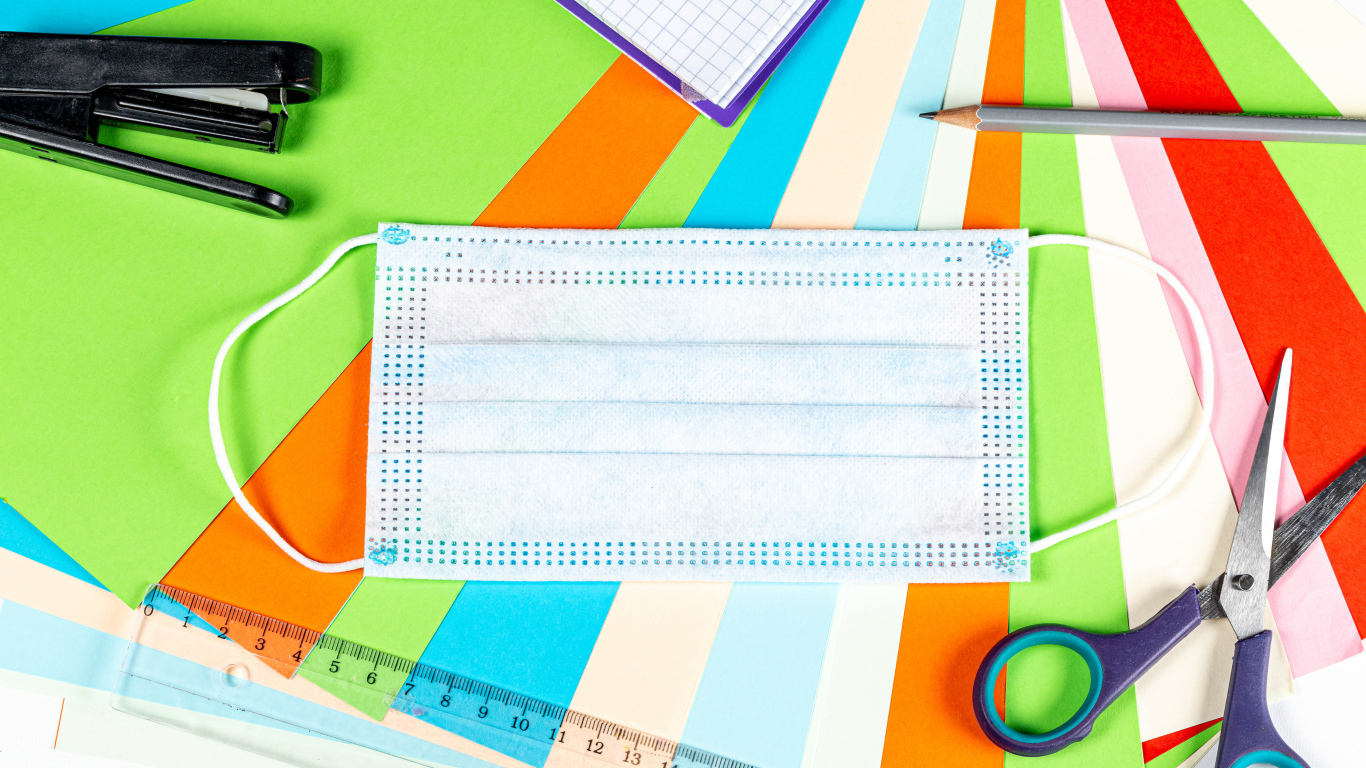 Маска от коронавируса лежит на цветной бумаге с канцелярскими предметами