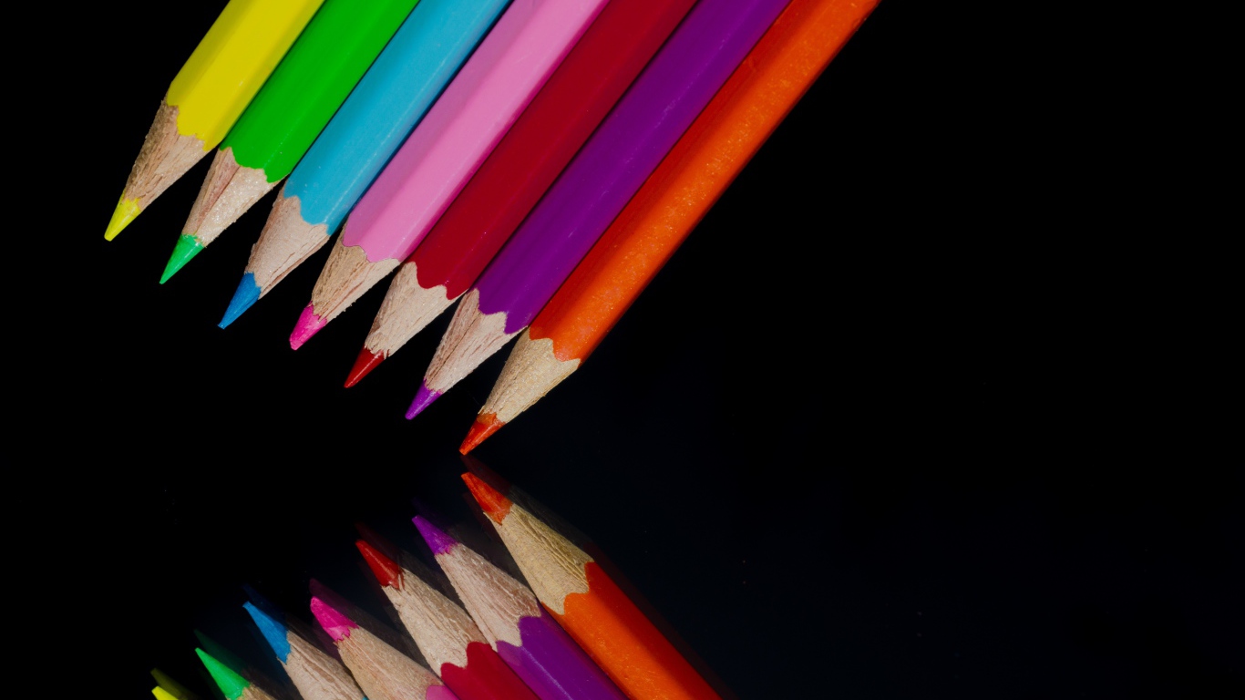 Multi-colored pencils are reflected in a black mirror surface