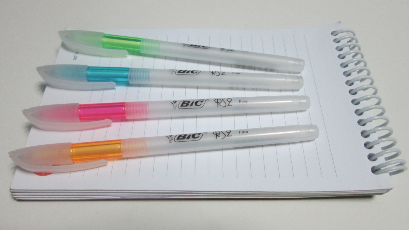 Разноцветные ручки лежат на блокноте на белом фоне 