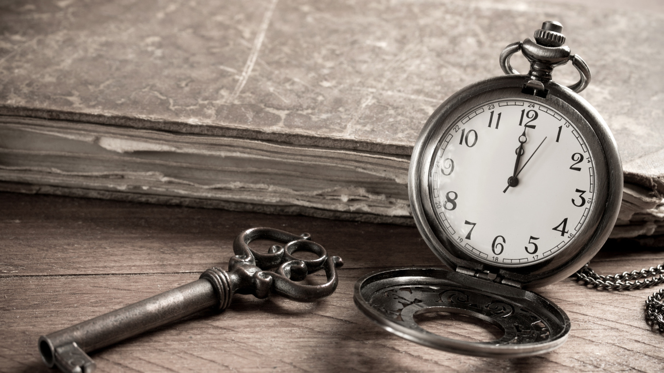 Карманные часы на столе с ключом и старой книгой 