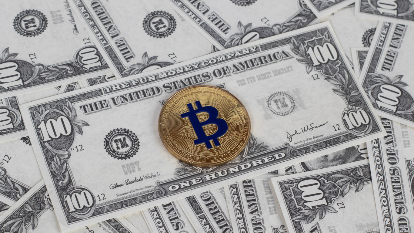Монета Биткоин лежит на стодолларовых купюрах