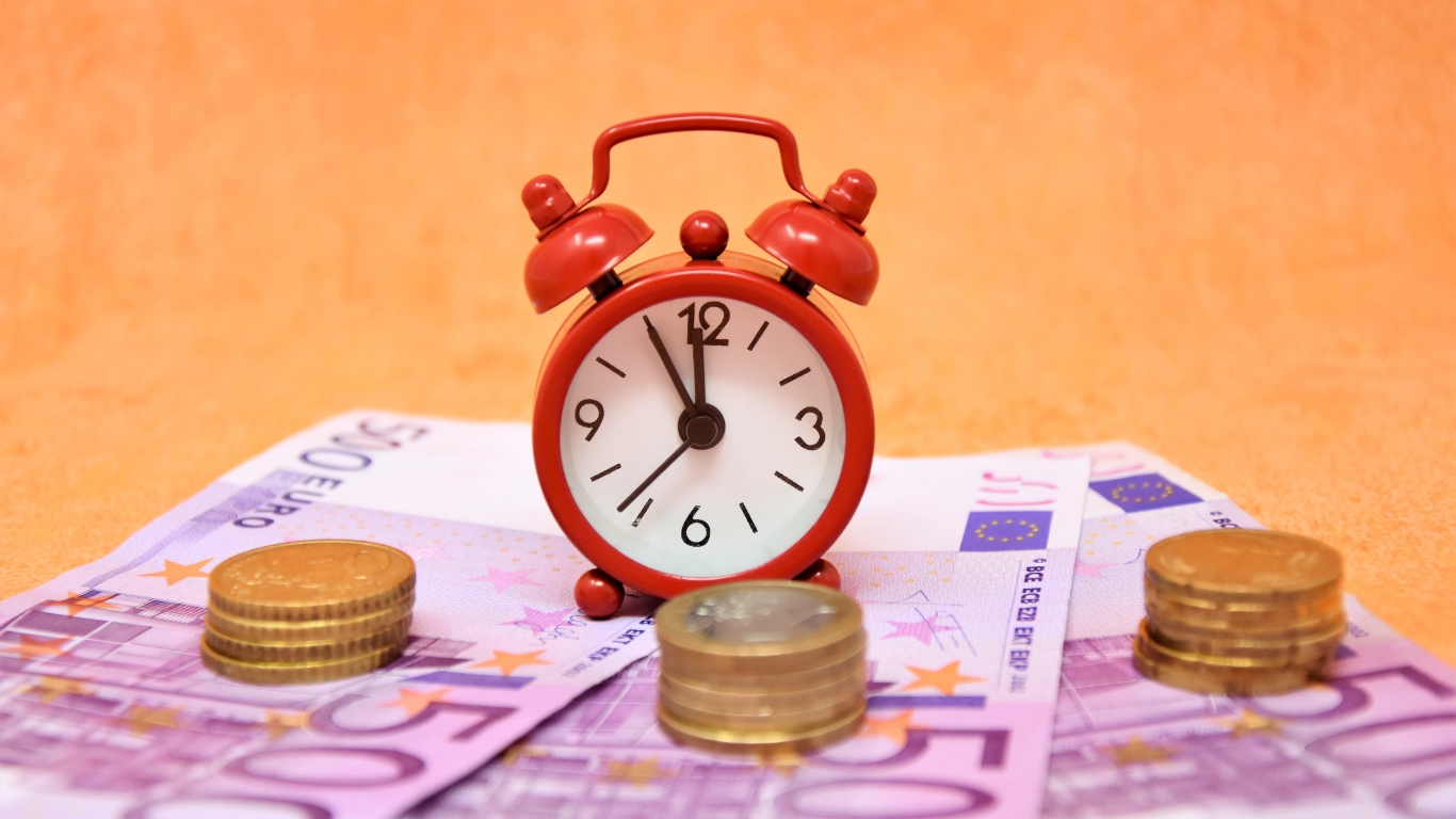 Маленький красный будильник с купюрами евро и монетами