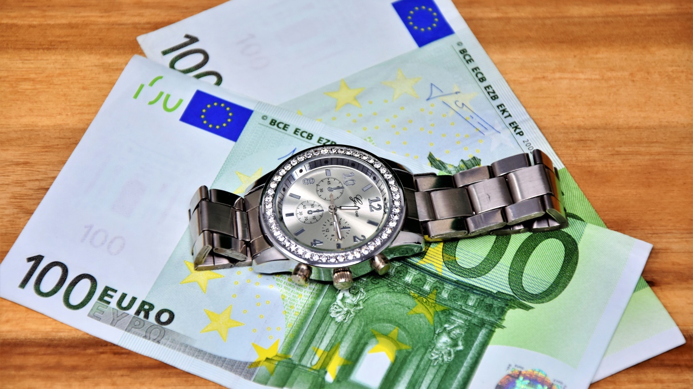 Две купюры по сто евро с часами на столе 