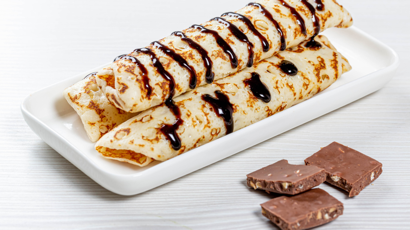 Аппетитные тонкие блины на белой тарелке с шоколадом