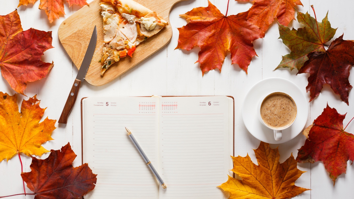 Ежедневник на столе с желтыми листьями, кофе и пиццей 