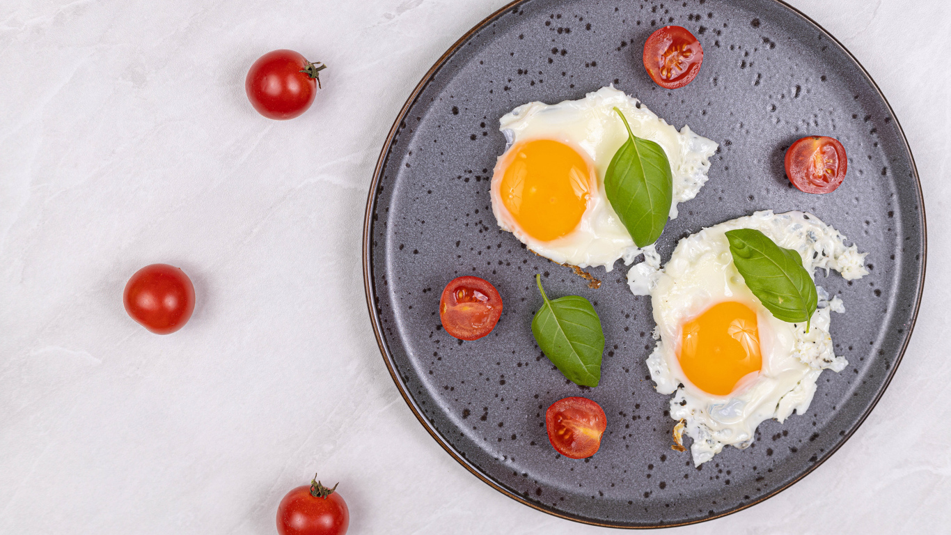 Яичница глазунья с помидорами и листьями базилика на черной тарелке 