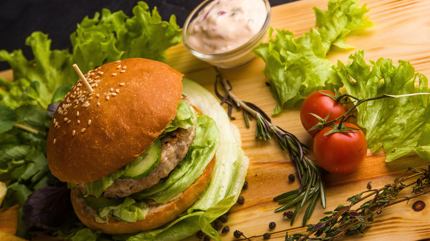 Гамбургер на столе с листьями салата, специями, помидорами и соусом