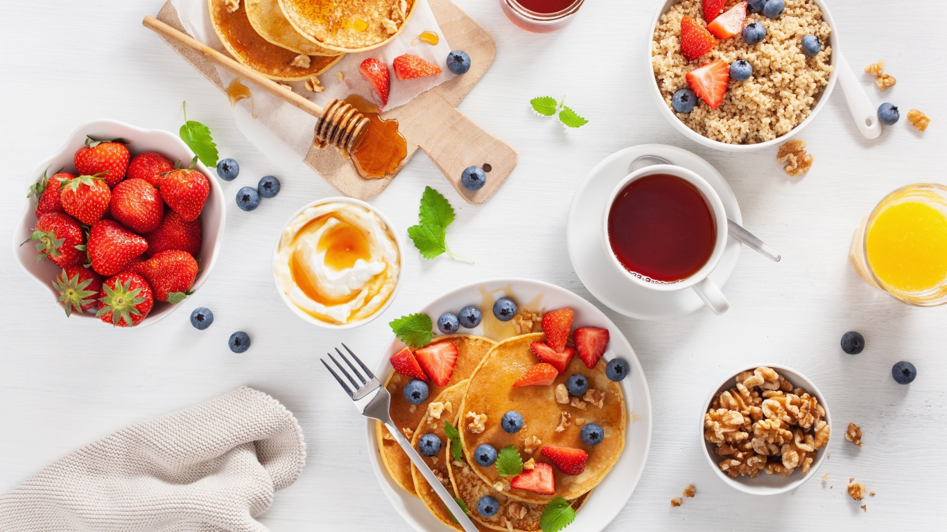 Pancakes with berries on a table with juice, tea and granola for breakfast