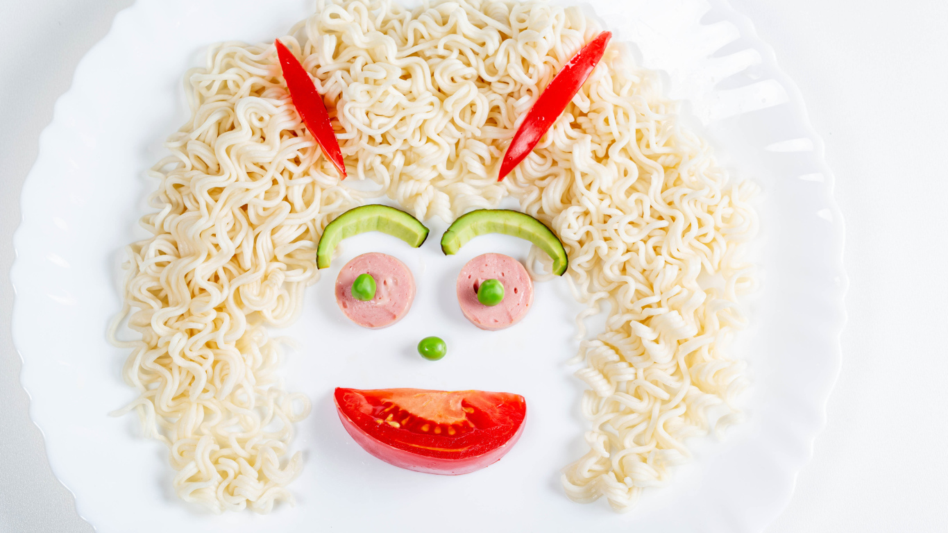 Лицо из вермишели с овощами и колбасой на белой тарелке 