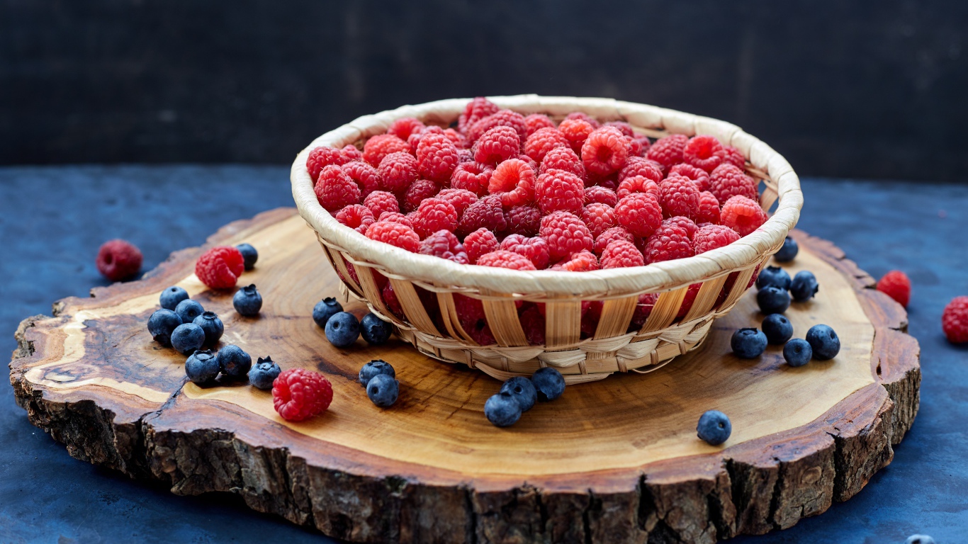 Корзинка с малиной на столе с ягодами черники