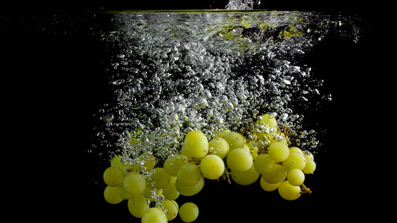 Ягоды белого винограда в воде на черном фоне