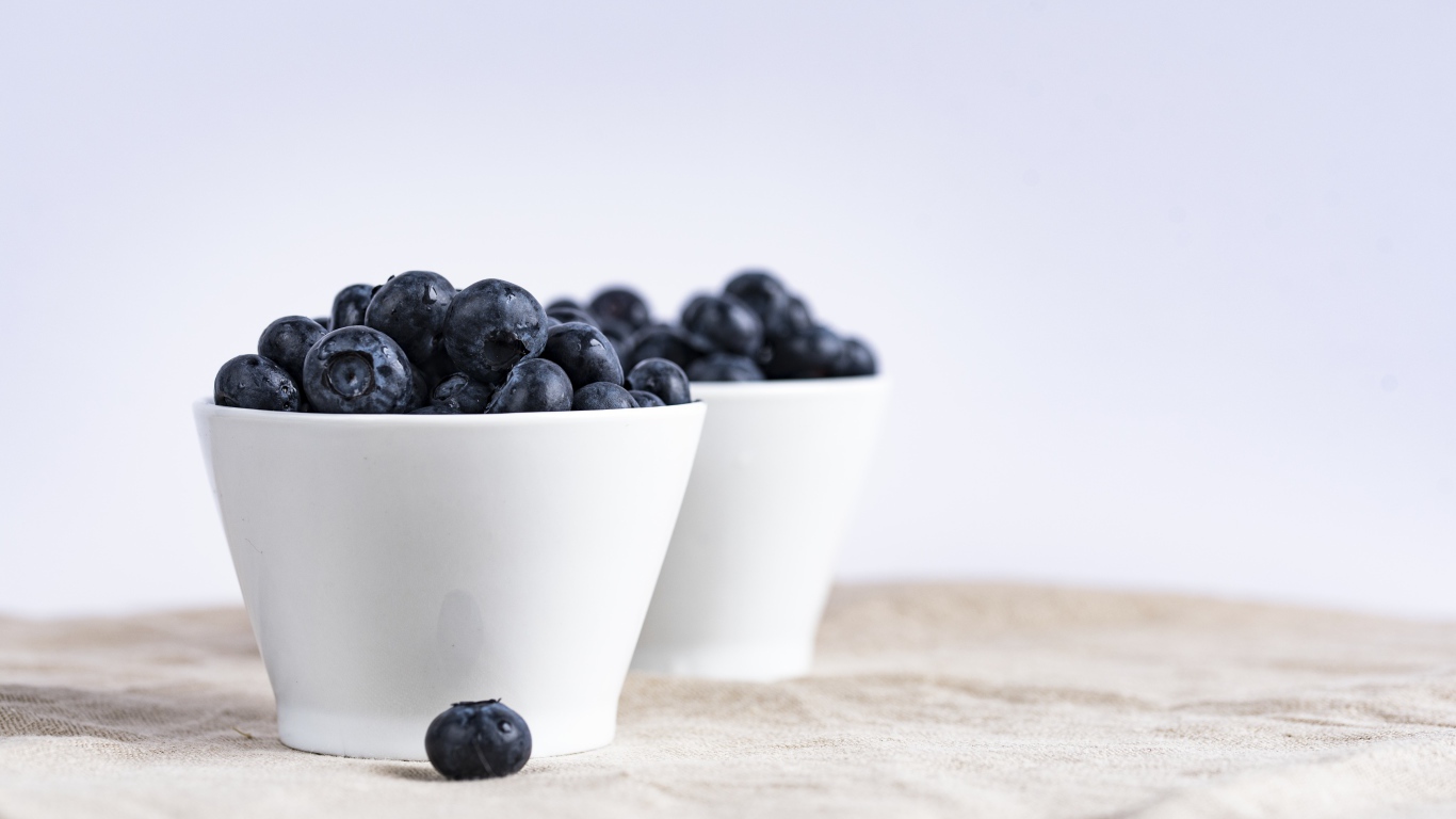 Синие ягоды черники в белой посуде на столе 