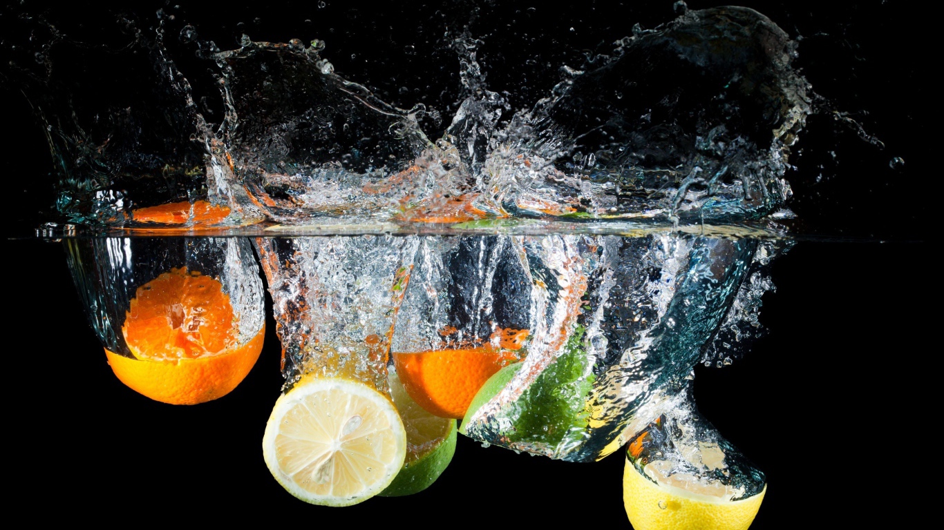 Цитрусовые фрукты падают в воду на черном фоне