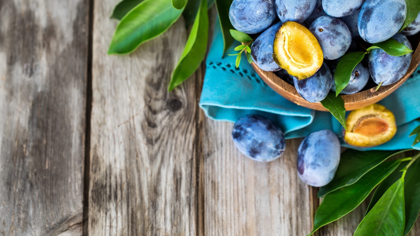 Свежие синие сливы с зелеными листьями на столе 