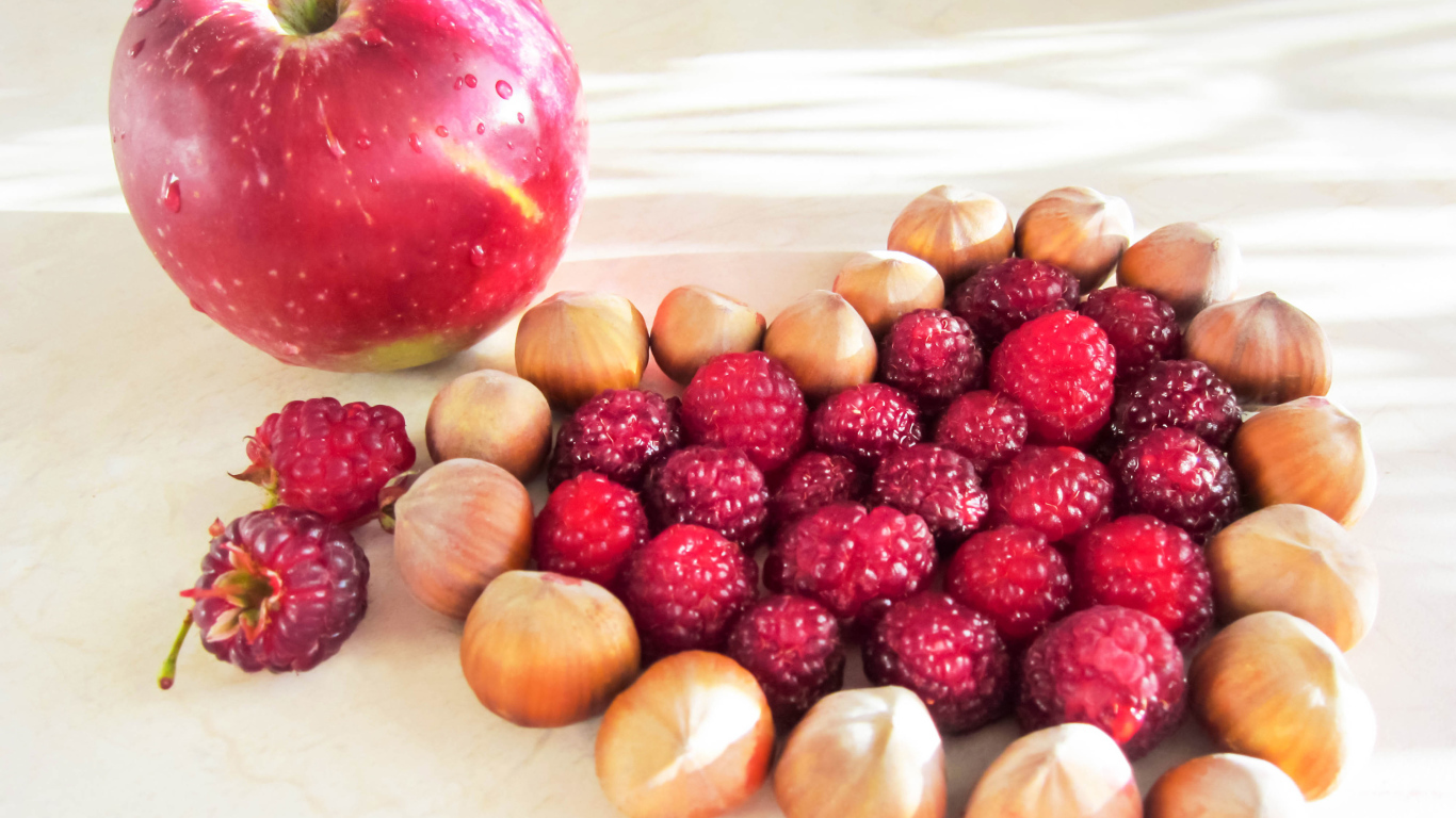 Сердце из лесных орехов и малины на столе с красным яблоком