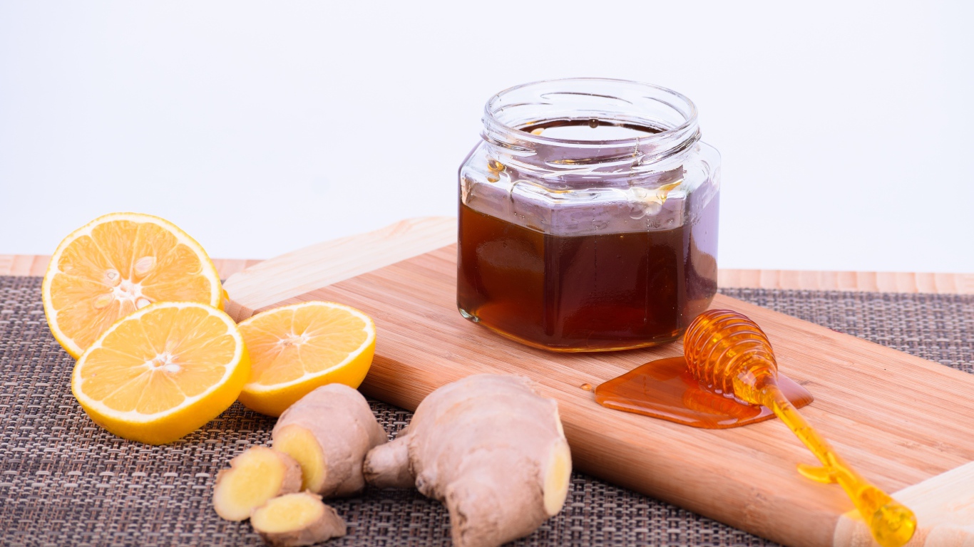 Jar of honey on a board with lemon and ginger root