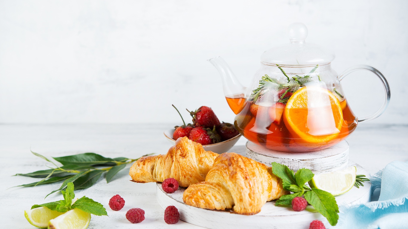 Kettle with lemon and strawberries on a table with croissants